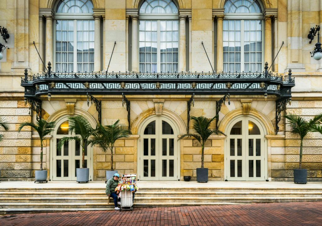 A lone vendor sits by a historic building with arched doorways in Bogotá, Colombia.