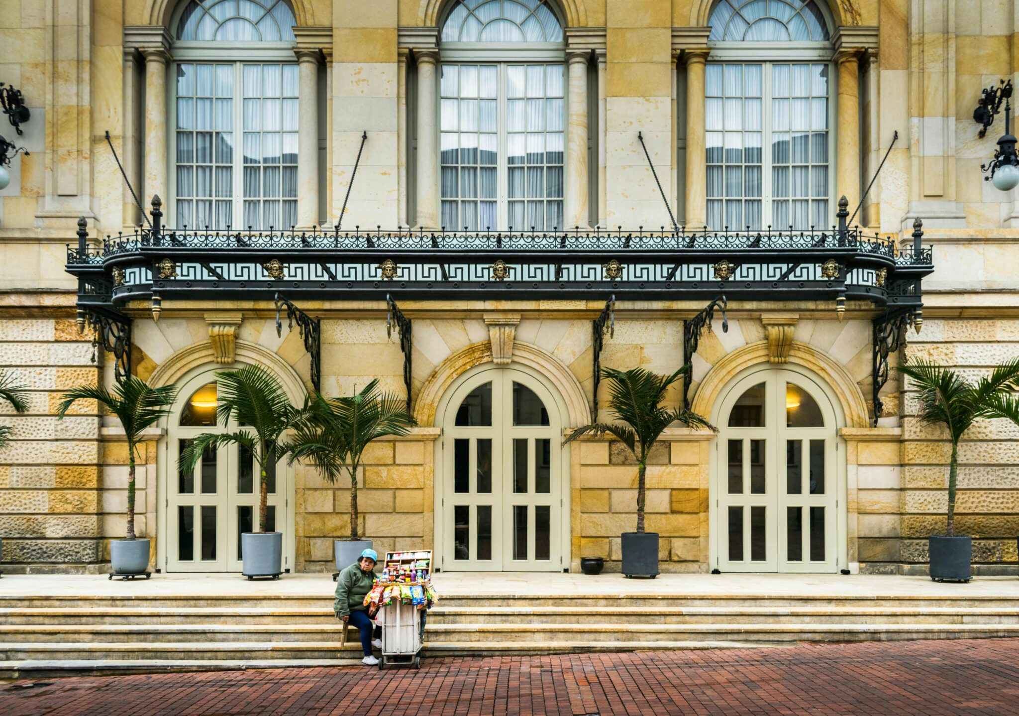 A lone vendor sits by a historic building with arched doorways in Bogotá, Colombia.