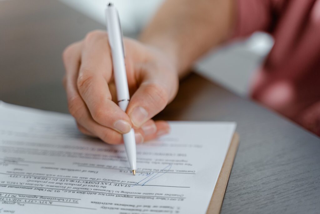 The Anatomy of a Colombian Contractor Agreement: 12 Clauses Every Foreign Company Should Understand Detailed view of a hand writing a signature on an official document with a ballpoint pen.