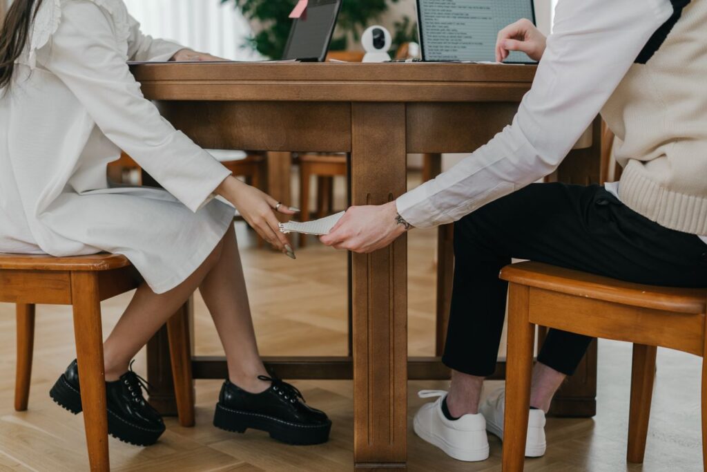 Two students covertly passing notes under a table during an exam indoors.